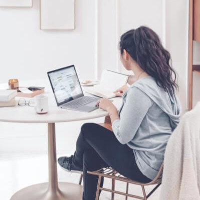 woman sitting at kitchen table typing on a laptio